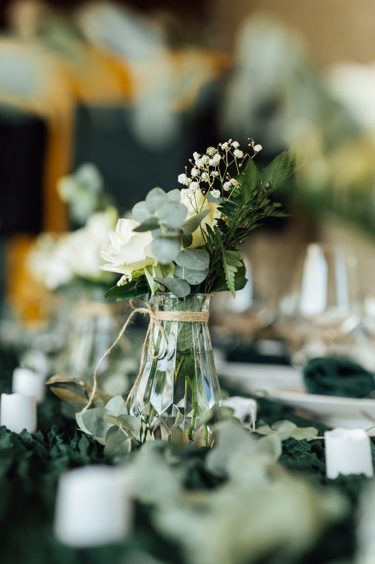 Stylish festive table setting with wine glasses, plates, green fabric napkins and floral decorations in natural sunlight