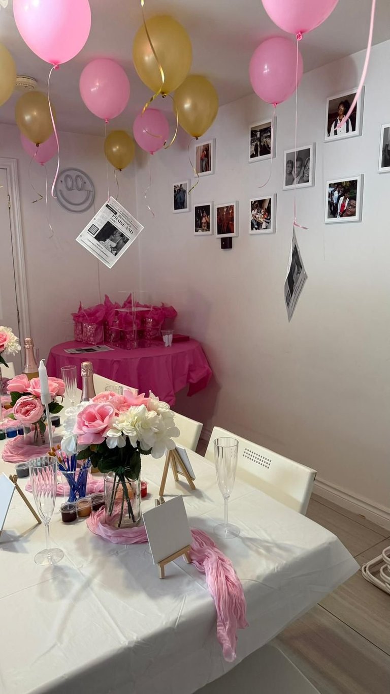 Pink and gold decorated party venue with balloons, photo display, white table with pink and white flowers, and hot pink accent table