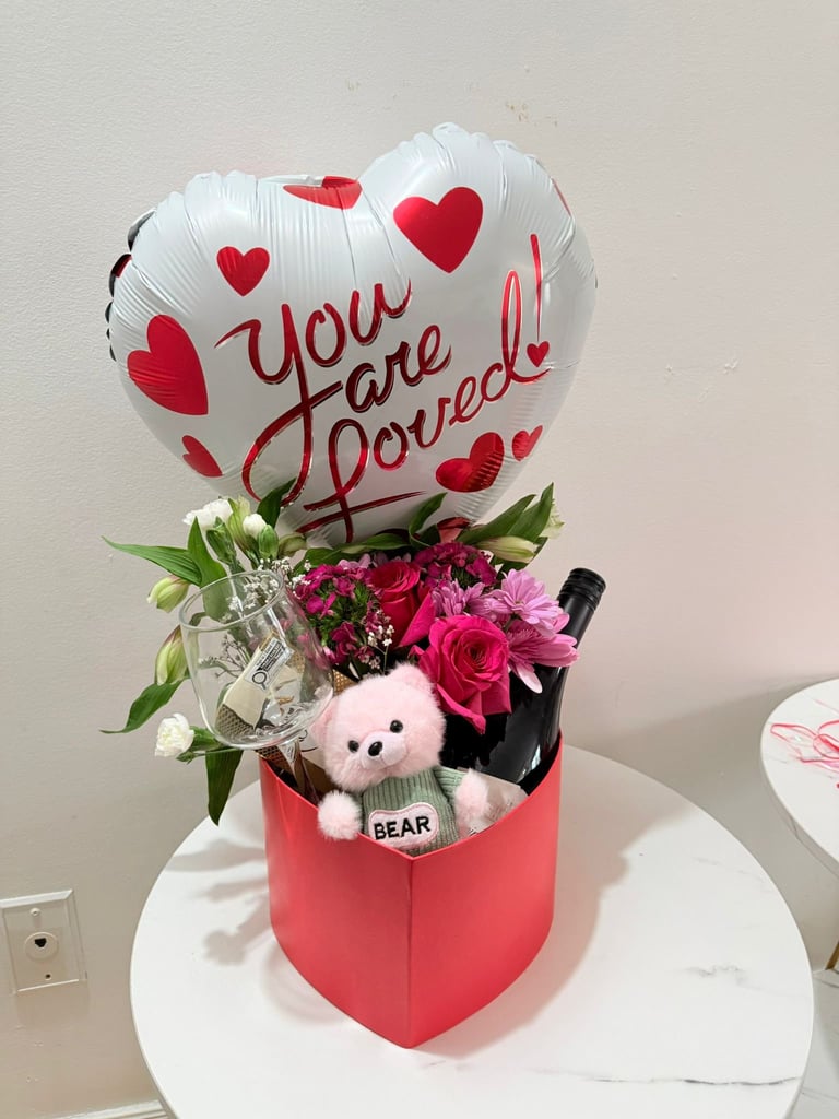 Love-themed gift arrangement with You are Loved heart balloon, red and pink roses, small teddy bear, and wine bottle in red box