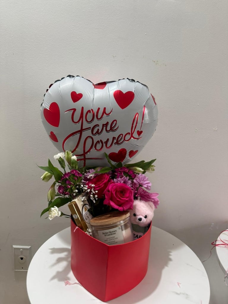 Heart-shaped You are Loved balloon with red roses and pink carnations in a red box on white table